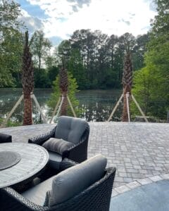 Outdoor patio setting with wicker furniture overlooking a tranquil lake with decorative torches in the background.