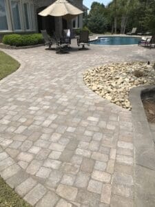 Paved patio area with a decorative stone border leading to a pool and outdoor furniture in the background.