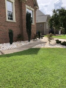 A suburban house with a landscaped yard featuring a walkway, trimmed bushes, and a decorative rock bed.