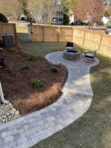 Well-manicured backyard with a curved stone pathway, mulched garden beds, a fire pit, and patio furniture.