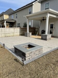 Backyard with a stone fire pit, paved patio, and a covered porch area of a suburban home.