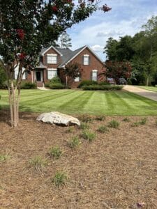 Brick house with landscaped yard, featuring a large rock and flowering trees.