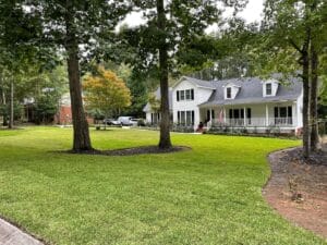 A spacious front yard with well-maintained green grass, surrounded by trees, in front of a two-story house with a white facade and porch.